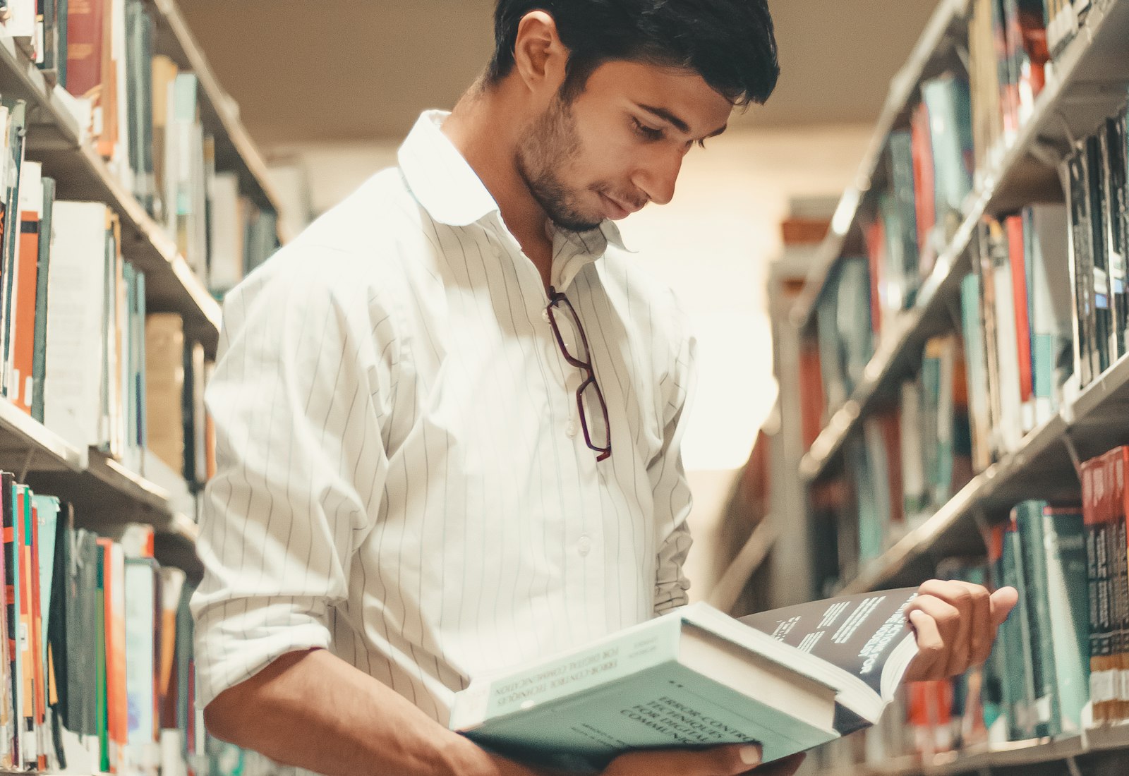 A UPSC aspirant reading a thick textbook between library shelves in India